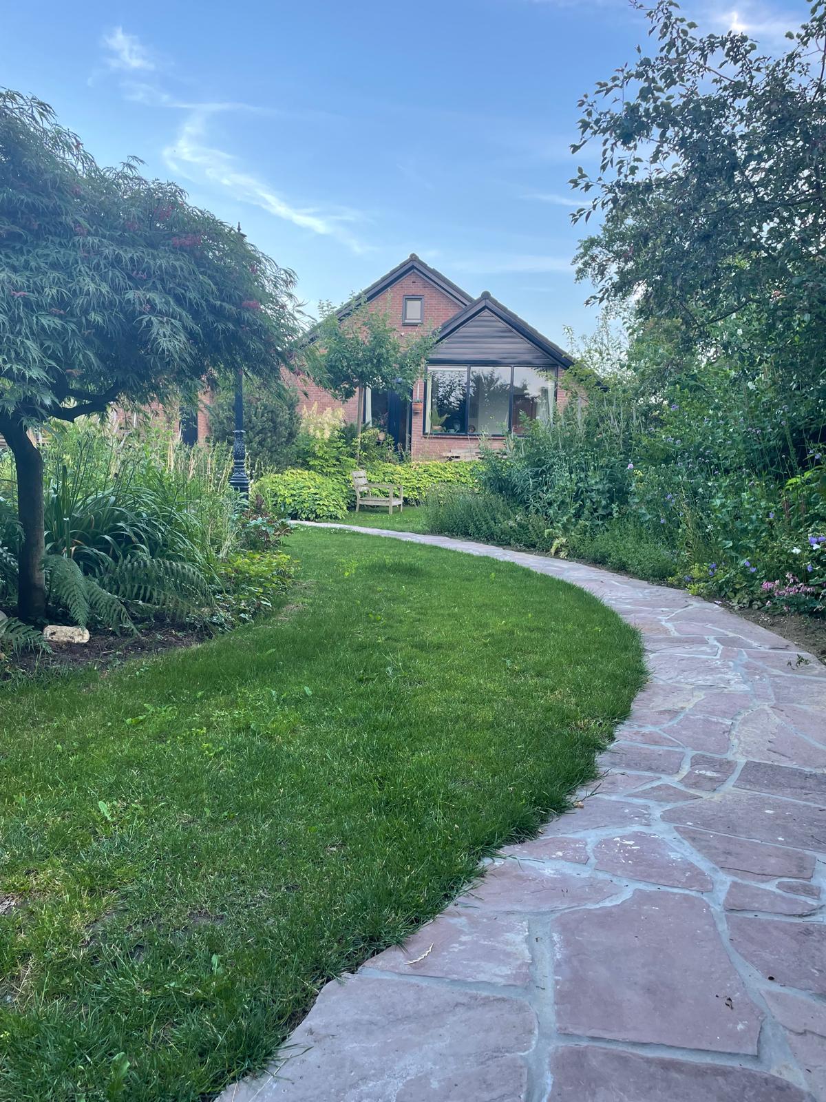 Prachtig voorbeeld van natuursteen verharding met organische vormen die harmonieus door de tuin slingert, omgeven door weelderige beplanting en perfect onderhouden gazon